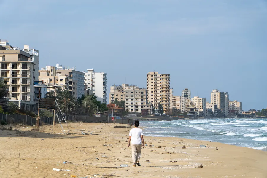 A man walking along the beach in front of the abandoned hotels of Varosha