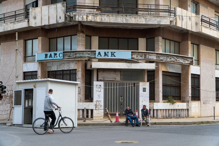 A bicycle passes a closed Barclays Bank branch with two men sitting outside