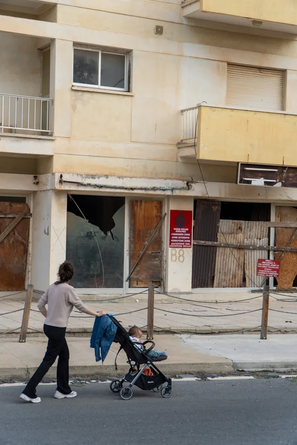 A woman pushes a pram past boarded-up shops and a forbidden-zone sign